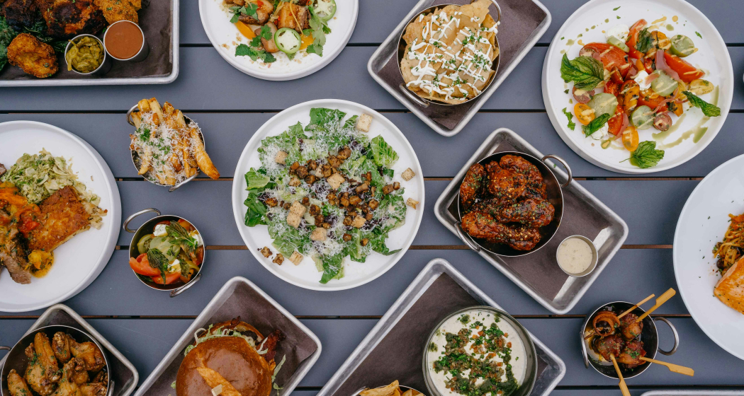 Draufsicht auf einen gedeckten Aussentisch mit vielfältigen Speisen: Salat, Chicken Wings, Nachos, Burger, Spiesse und Dips – bereit für den Inside Labs Summer Grill in Flims.