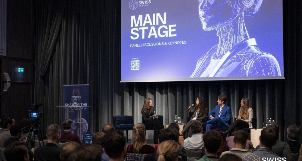Publikum bei einer Podiumsdiskussion des Swiss AI Summit mit vier Personen auf der Bühne vor einer Leinwand mit der Aufschrift Main Stage, Panel Discussions & Keynotes