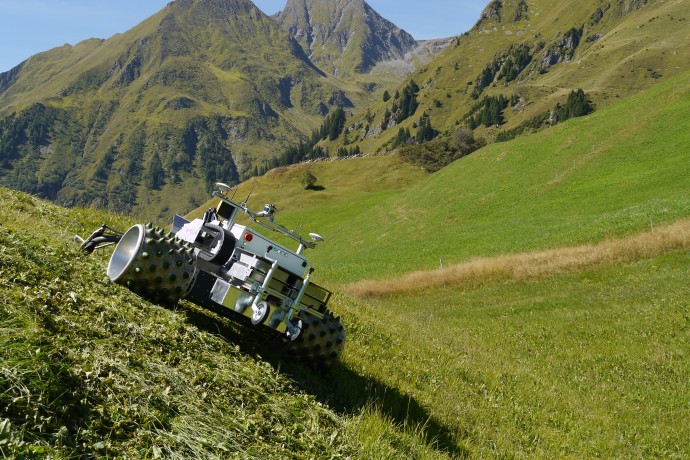 Elektrisch betriebener Einachser «AMEA» auf einer grünen Hangwiese vor alpiner Bergkulisse bei sonnigem Wetter.