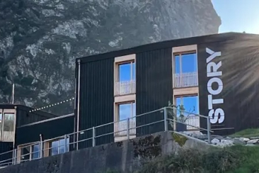 Aussenansicht des Story Thusis vor Bergkulisse bei Sonnenschein, mit moderner dunkler Holzfassade und vertikalem «STORY»-Schriftzug am Gebäude.