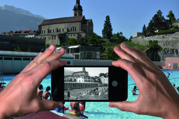 Zwei Hände halten ein Smartphone vor das heutige Freibad Sand in Chur. Auf dem Handydisplay ist ein historisches Schwarz-Weiss-Foto derselben Anlage zu sehen, mit Badenden im Wasser und dem Turm der Kathedrale St. Maria Himmelfahrt im Hintergrund. Die Gegenüberstellung zeigt den Wandel des Freibads Sand über Jahrzehnte, während die Kathedrale und die Bündner Bergkulisse als unverkennbare Wahrzeichen erhalten geblieben sind. Bild: Fotostiftung Graubünden / Pictomap-Projekt.