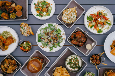 Draufsicht auf einen gedeckten Aussentisch mit vielfältigen Speisen: Salat, Chicken Wings, Nachos, Burger, Spiesse und Dips – bereit für den Inside Labs Summer Grill in Flims.